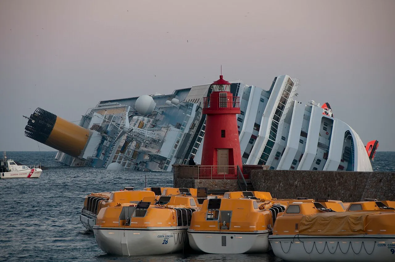 Costa Concordia lying on its side near Giglio, with lifeboats in the foreground.